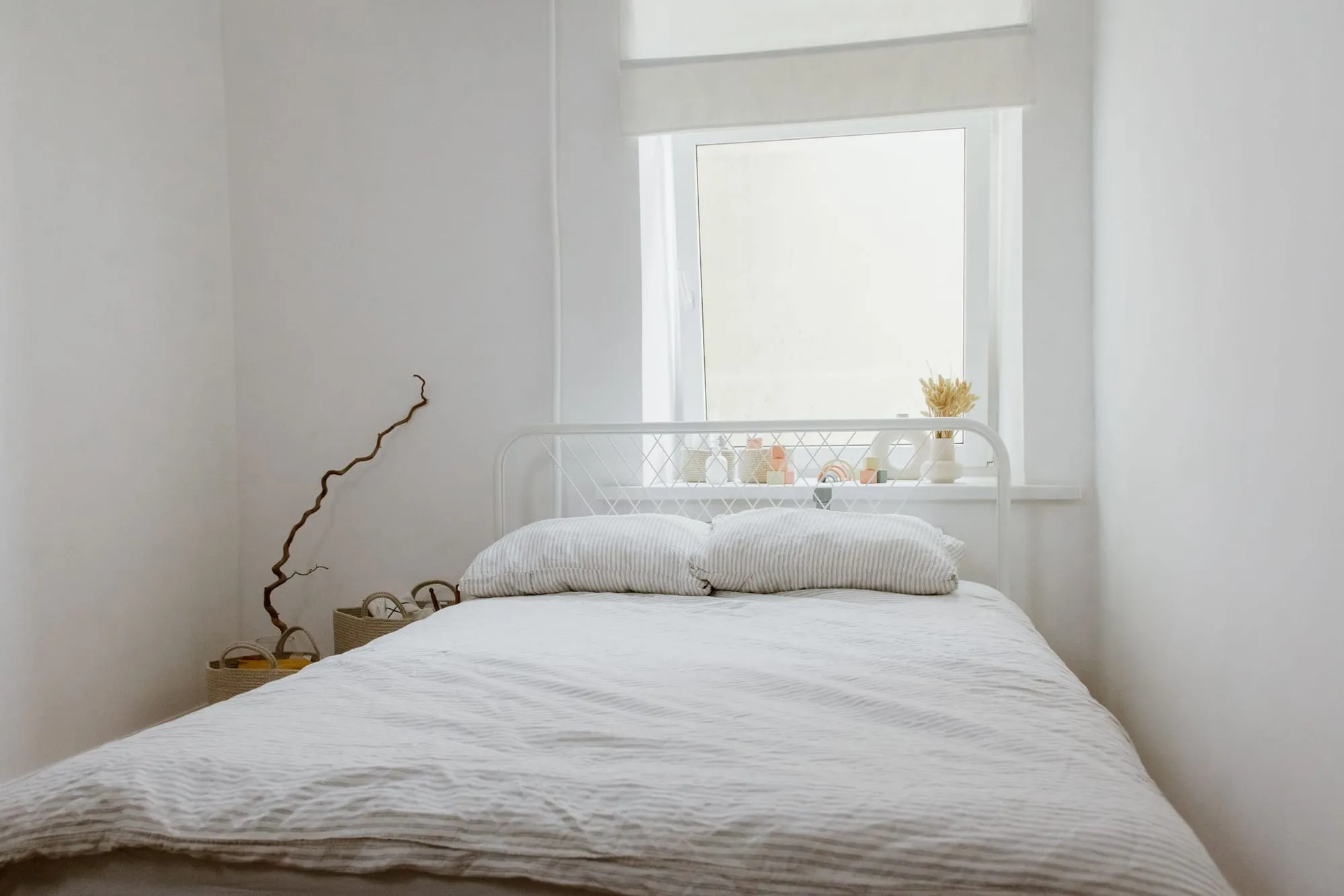 Weißes Schlafzimmer mit Bett unter dem Fenster im weichen Tageslicht
